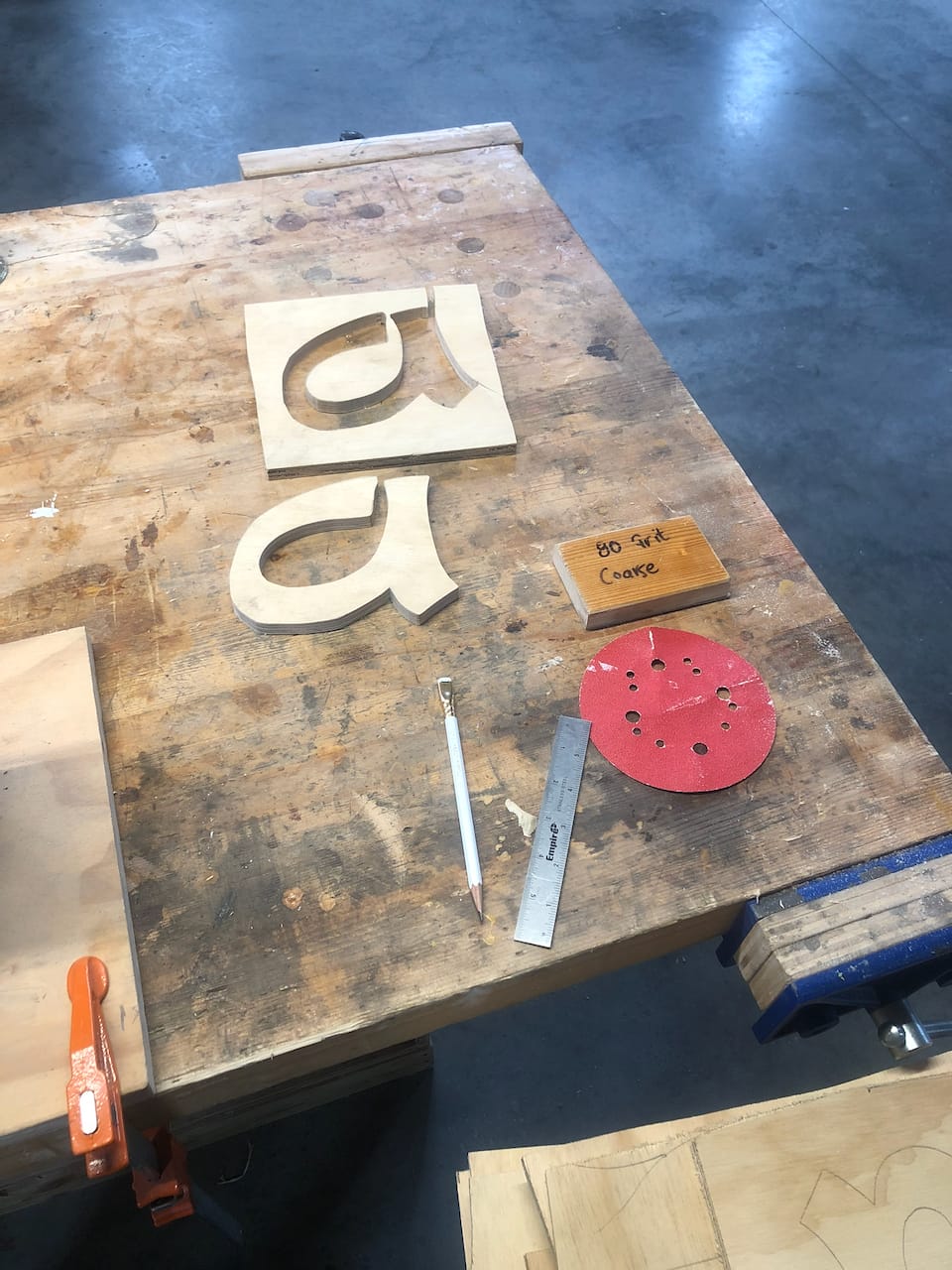 Cut letters, a template, and the coarse sanding disc on the bench.