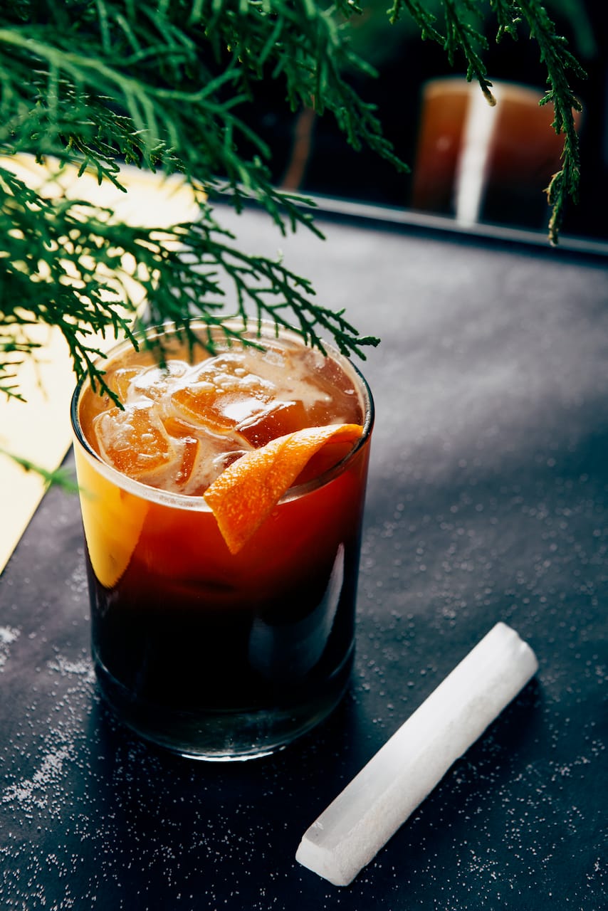A cocktail with an orange twist and a sprig of cedar.